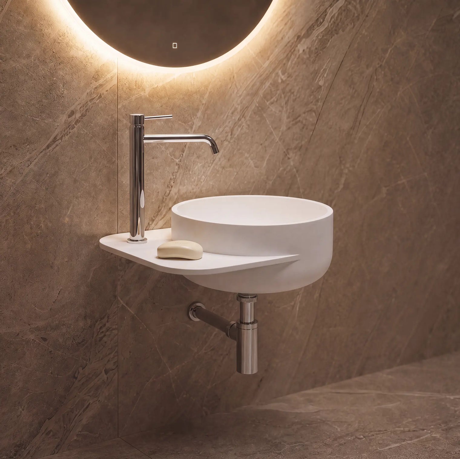 A modern wall-mounted white vessel sink with a chrome faucet, set against a brown stone-look tiled wall with an illuminated round mirror above.