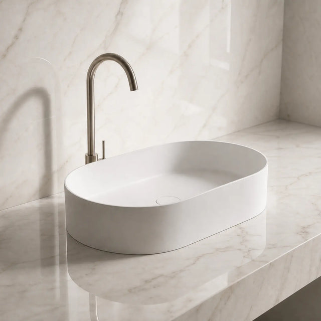 White Solid Surfaces oval sink on a marble countertop with a matching wall.