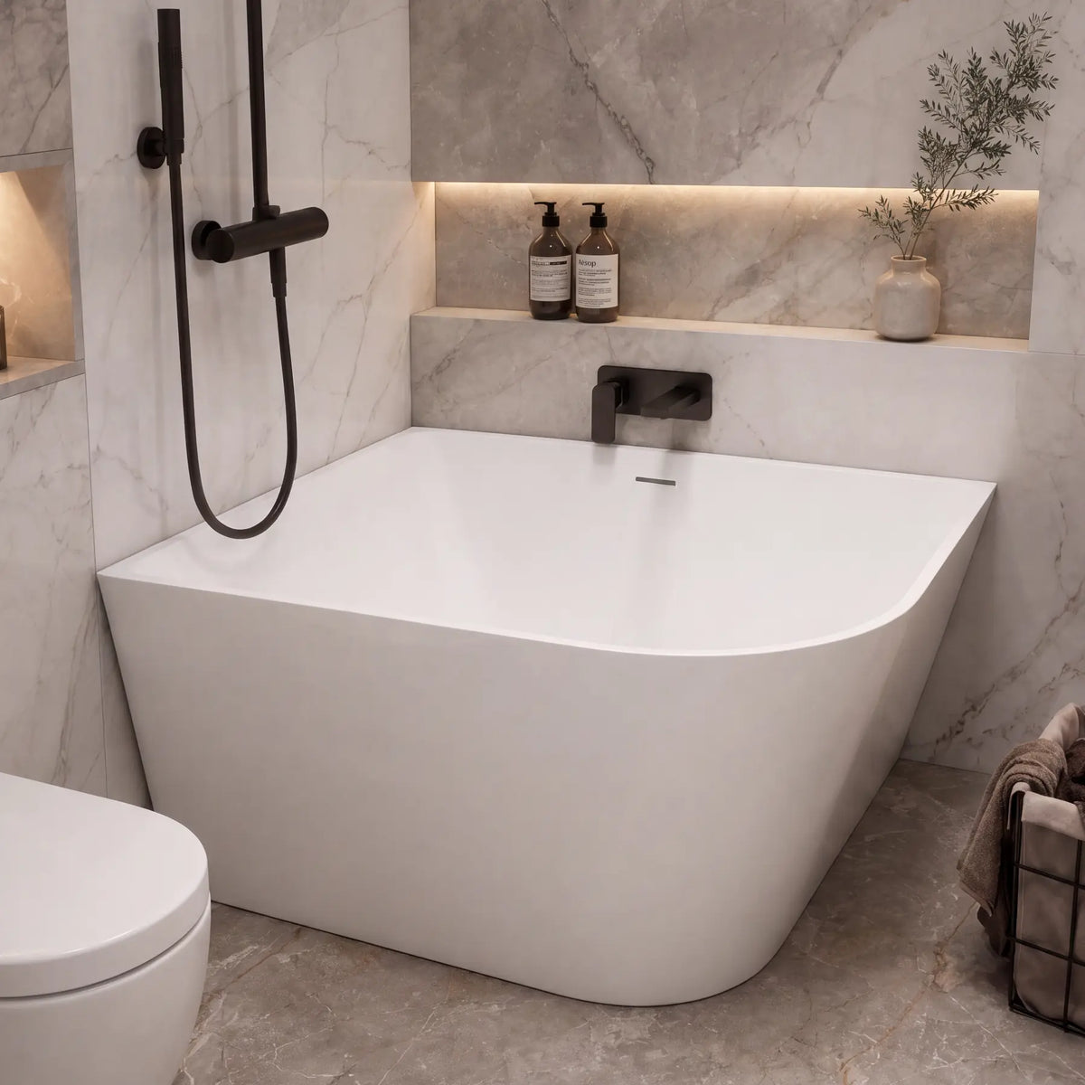 A modern freestanding bathtub in a marble-look bathroom with a black handheld shower, toilet, built-in shelves, and small decorative bottles.