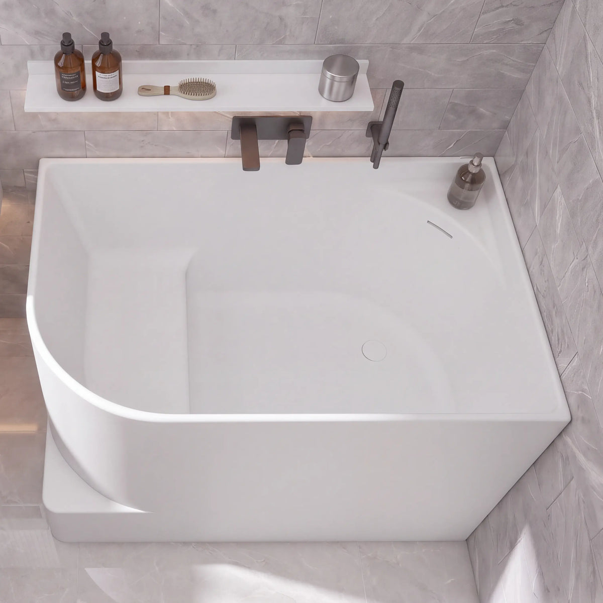 A modern bathroom scene with a large white freestanding bathtub, a white wall-mounted sink, gray stone tile walls and floor, and a few small bathroom accessories and towels.