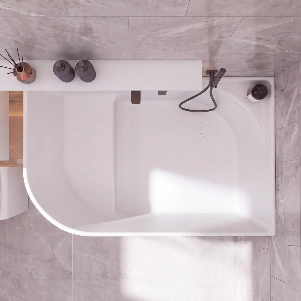 A modern white freestanding bathtub with a matte black handheld shower and faucet, shown from a top-down view in a tiled bathroom with gray stone-look tiles.