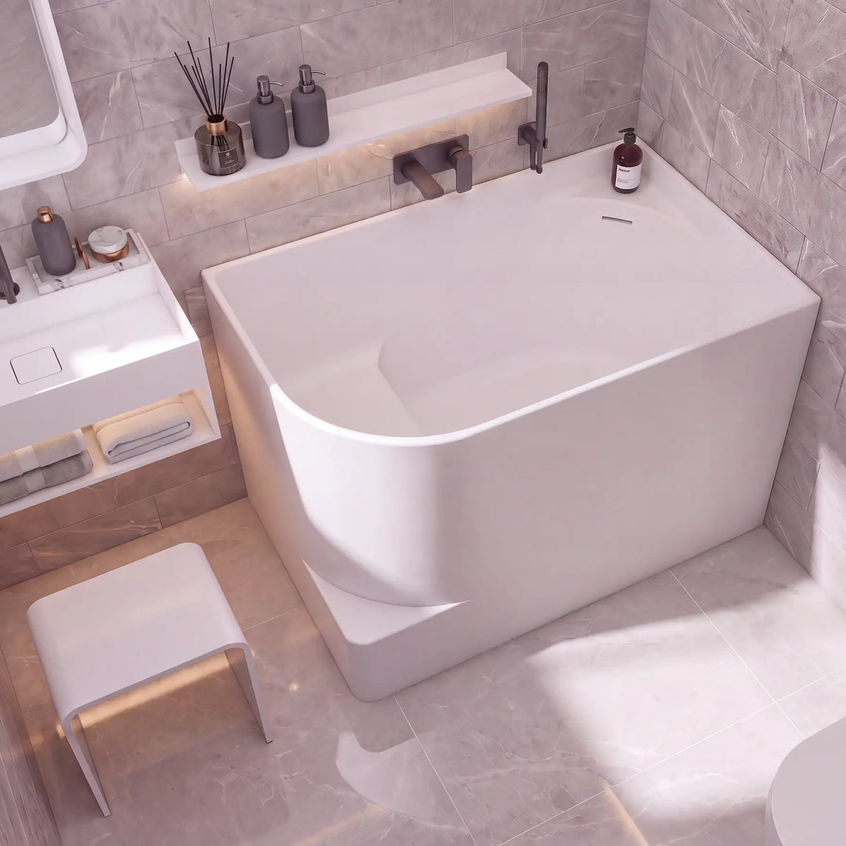 A modern freestanding bathtub in a minimalist bathroom setting with gray marble-look tiled walls and floor, a white vanity, and a small white stool.