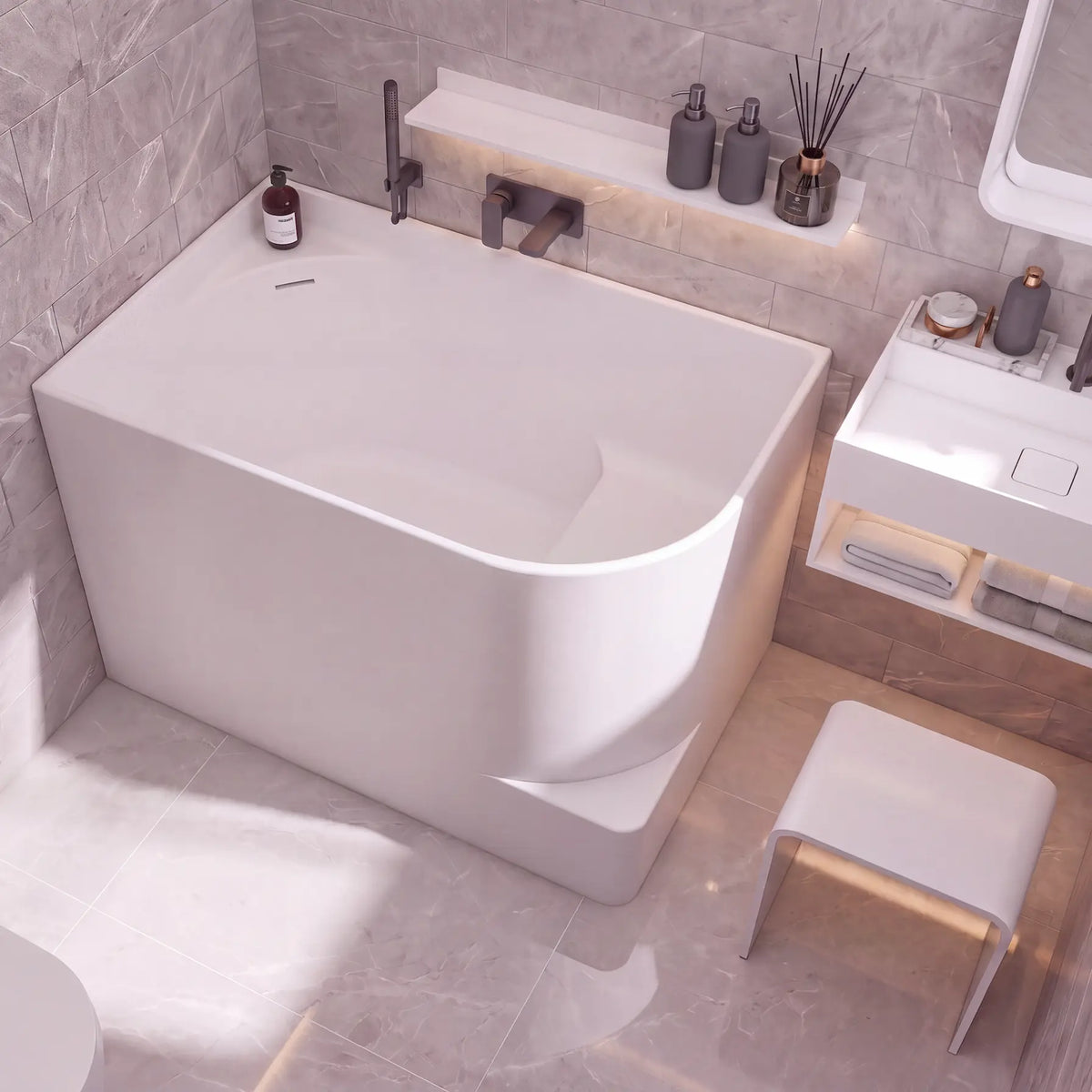 A modern freestanding bathtub in a minimalist bathroom setting with gray marble-look tiled walls and floor, a white vanity, and a small white stool.