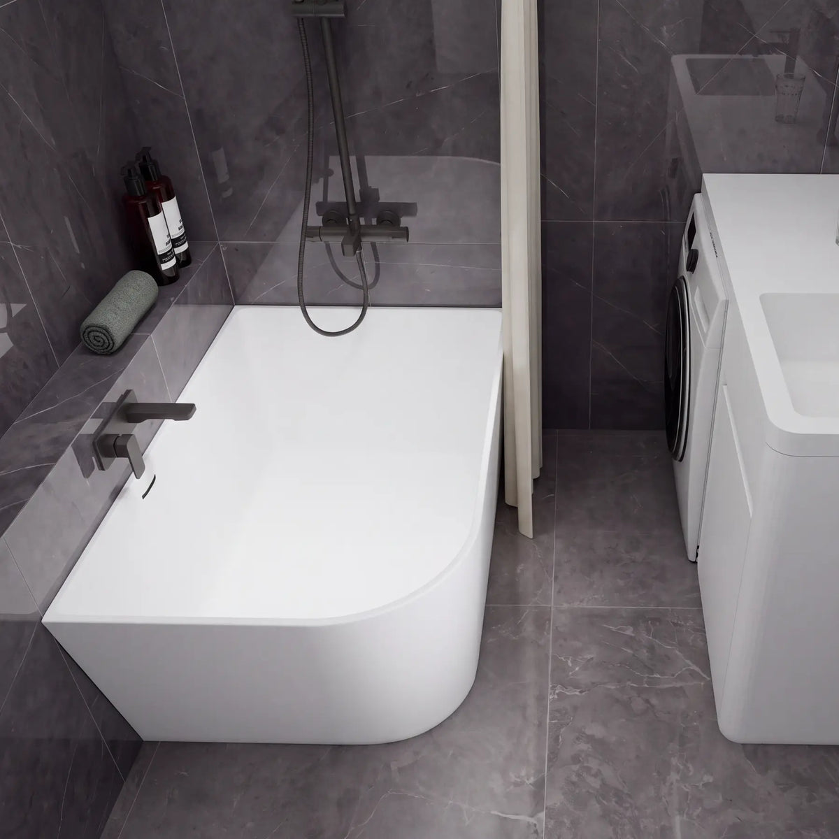 A modern bathroom setup featuring a white freestanding bathtub with a dark wall-mounted faucet and shower system, alongside a white sink vanity with a matching dark faucet and a small washing machine, all set against dark gray tiled walls and floor.