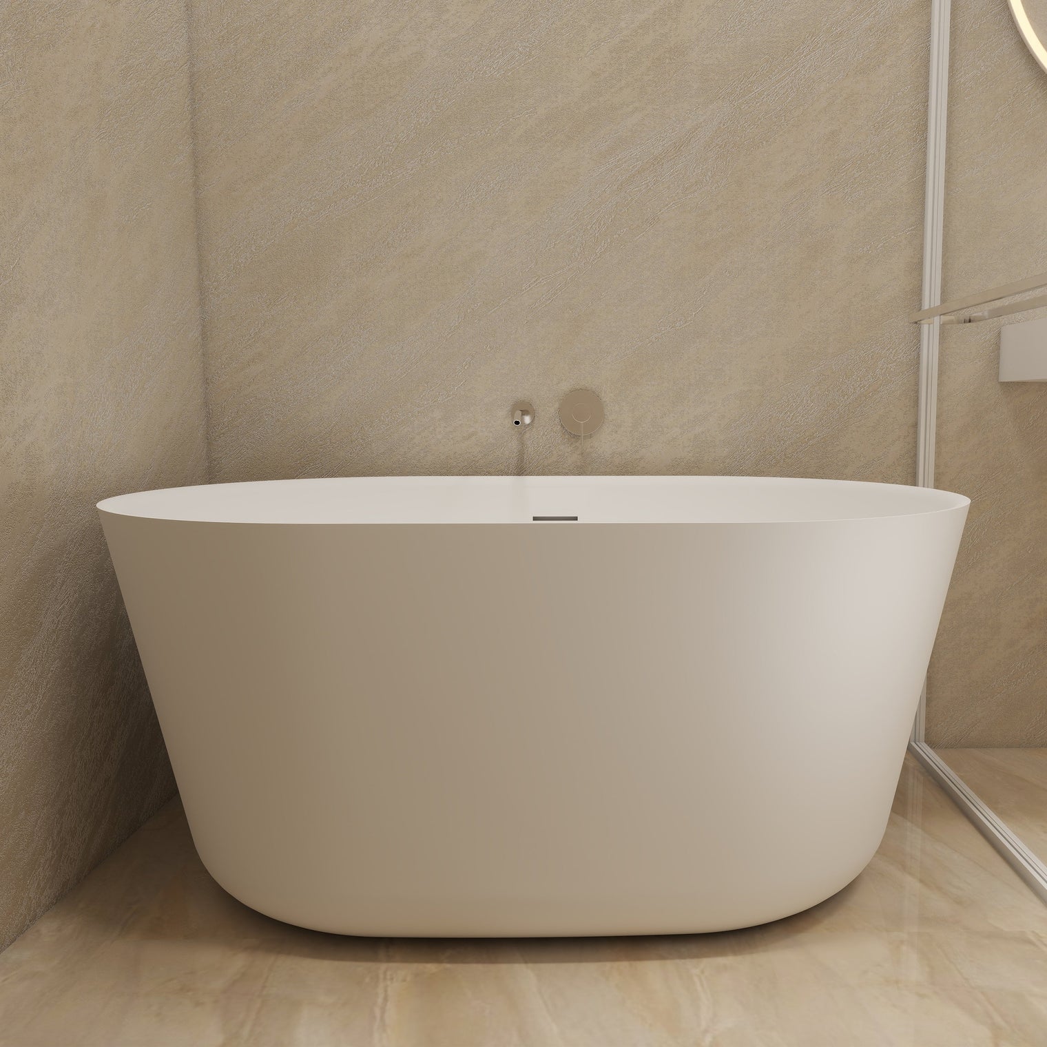 A modern freestanding oval bathtub in matte white, set in a minimalist bathroom with beige stone walls and floor, next to a glass shower screen.