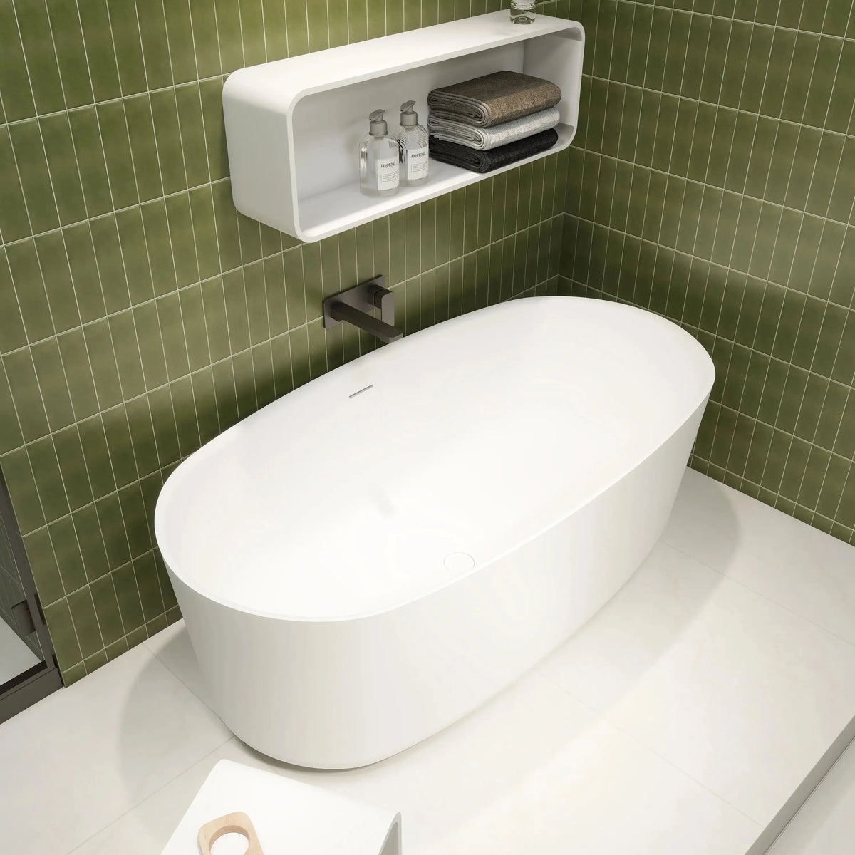 Modern white freestanding bathtub in a bathroom with green tiled walls.