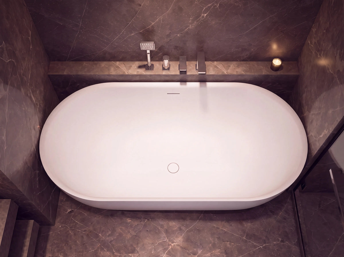 A freestanding oval bathtub in white, set into a dark marble-tiled bathroom with a built-in shelf holding a chrome faucet and shower head.