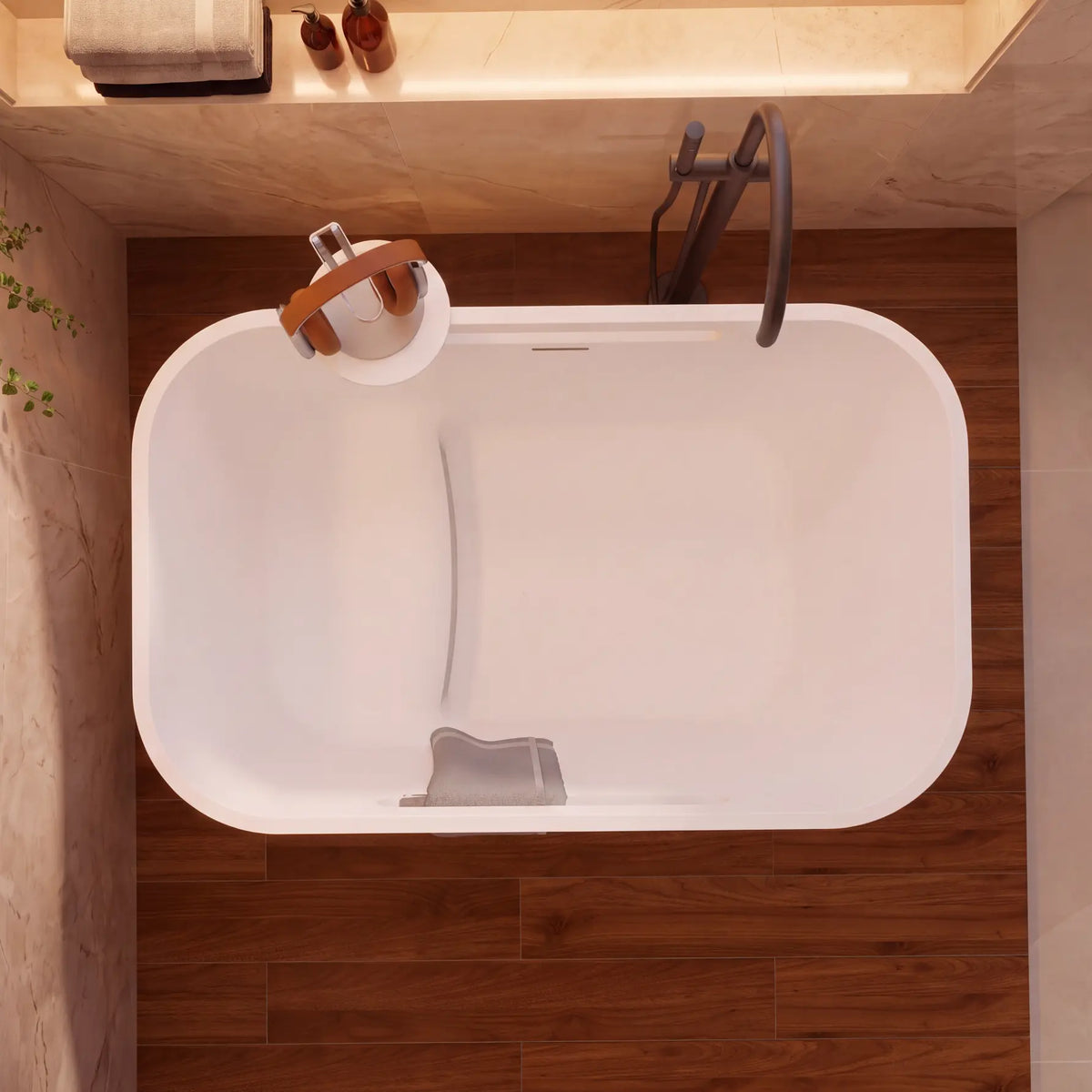 A top-down view of a modern freestanding bathtub in a bathroom setting with dark wood flooring, beige walls, and a dark faucet.