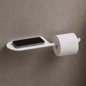 Wall-mounted toilet paper holder with smartphone tray in a bathroom setting.