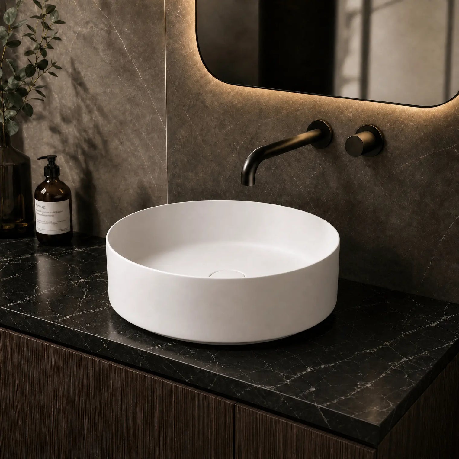 White round sink on a dark marble countertop with a mirror and bottles in the background.