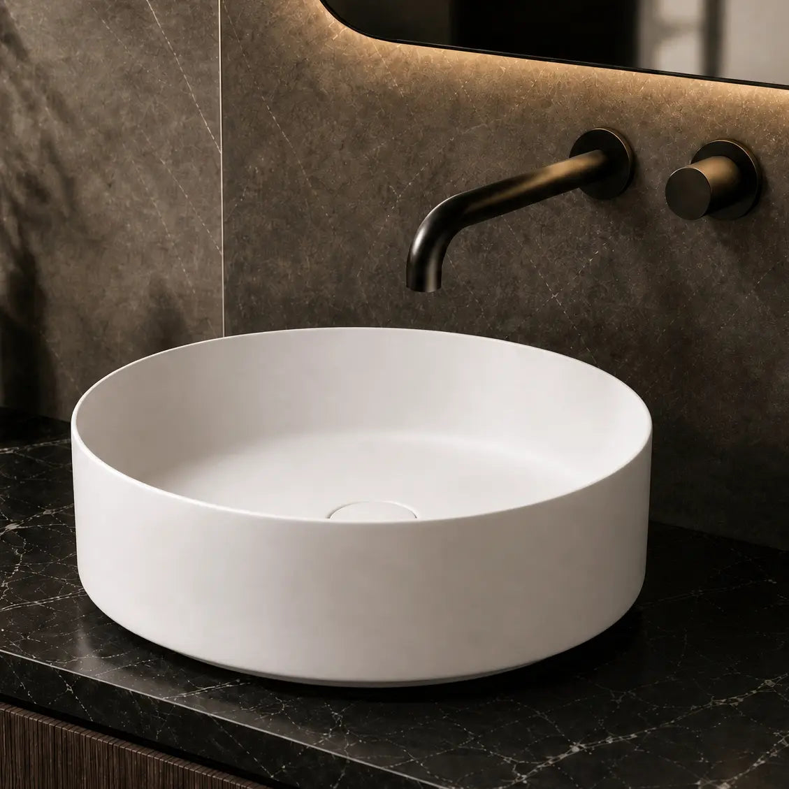 White round sink on a dark marble countertop with a mirror and bottles in the background.