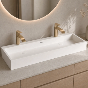 Bathroom vanity with white rectangular sink, gold faucets, and decorative elements.