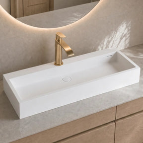 Modern bathroom vanity with a white sink and gold faucet.