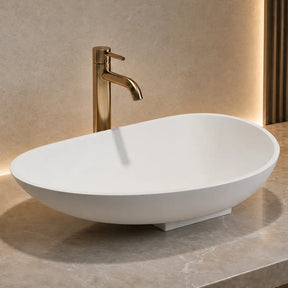 White oval Solid Surfaces sink with gold faucet on a marble countertop in a bathroom setting.