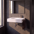 A modern wall-mounted white sink with a chrome faucet, set against dark gray marble-look tiled walls in a bathroom. A rectangular mirror is mounted above the sink, and a dark brown towel hangs from the side.