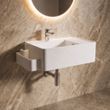 A modern white rectangular wall-mounted sink with a chrome faucet and side holder, installed on a beige marble-look wall beneath a lit round mirror.