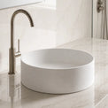 Modern bathroom with a round solid surfaces white sink and bronze faucet on a marble countertop.