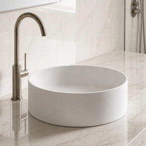 Modern bathroom with a round solid surfaces white sink and bronze faucet on a marble countertop.