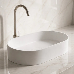 White Solid Surfaces oval sink on a marble countertop with a matching wall.
