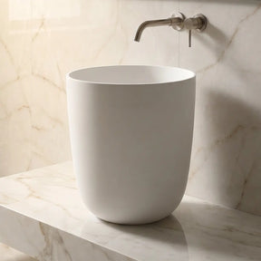 White freestanding sink on a marble countertop with a neutral-toned wall in the background