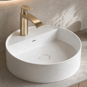 White round sink with gold faucet on a bathroom counter.