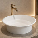 White round Solid surfaces sink with gold faucet on a marble countertop in a bathroom setting.