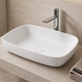 Modern bathroom with a white solid surfaces sink on a stone countertop, mirror, and towels.