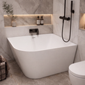 A modern freestanding bathtub in a marble-look bathroom with a black handheld shower, toilet, built-in shelves, and small decorative bottles.
