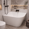 A modern freestanding bathtub in a marble-look bathroom with a black handheld shower, toilet, built-in shelves, and small decorative bottles.
