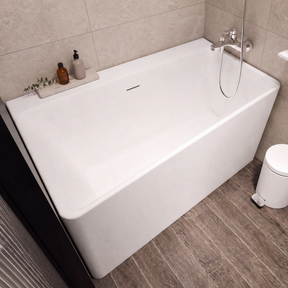 A modern freestanding white bathtub in a tiled bathroom with dark wood-look flooring, wall-mounted floating shelves, a small trash can, and a toilet visible at the right edge.