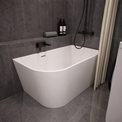 A modern freestanding bathtub with a curved corner design, shown installed in a bathroom with dark gray tiled walls and floor. The tub is white with matte black fixtures, including a wall-mounted faucet and shower system.