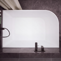 A modern freestanding rectangular bathtub with rounded corners, shown installed against dark gray tiled walls and floor. The tub is matte white, with matte black fixtures mounted on the right side and a matching black faucet centered at the bottom.
