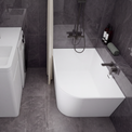 A modern bathroom setup featuring a white freestanding bathtub with a dark wall-mounted faucet and shower system, alongside a white sink vanity with a matching dark faucet and a small washing machine, all set against dark gray tiled walls and floor.
