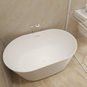 A modern freestanding oval bathtub in white, shown installed in a minimalist bathroom with beige textured walls and light wood flooring.