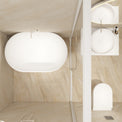 A modern bathroom interior with a large oval freestanding bathtub on the left, a glass shower enclosure, a wall-mounted white sink with a round basin and chrome faucet on the right, a white toilet below, and beige marble-look tiled walls and floor.