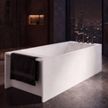A modern freestanding rectangular bathtub in matte white, shown in a luxurious dark-toned bathroom with a city skyline visible through large windows at night.