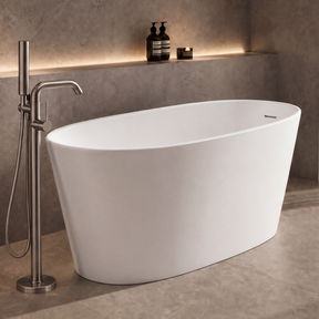 A modern freestanding oval bathtub in matte white, shown in a minimalist bathroom setting with a chrome floor-mounted faucet, textured gray walls, and a large window with sheer curtains.