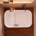 A top-down view of a modern freestanding bathtub in a bathroom setting with dark wood flooring, beige walls, and a dark faucet.