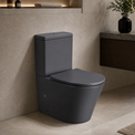 A matte dark gray 2-piece toilet in a modern bathroom setting with beige walls, a floating dark wood vanity, and a stone countertop.