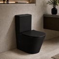 A matte black 2-piece toilet with a matching closed lid, shown installed in a modern bathroom with beige stone walls and a floating dark wood vanity.