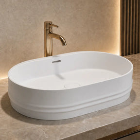 White oval Solid Surfaces sink on a gray countertop with a gold faucet in a modern bathroom setting.