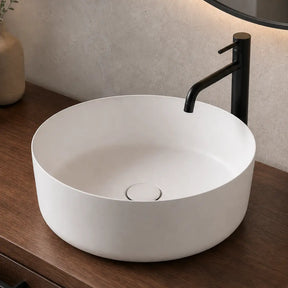White round sink on a wooden vanity with a black faucet, mirror, and decorative items.