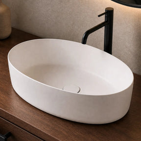 White oval sink on a wooden vanity with a black faucet, mirror, and decorative items.