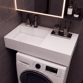 A modern bathroom vanity setup with a white integrated sink and washing machine cabinet, set against dark gray tiled walls under a lit mirror.