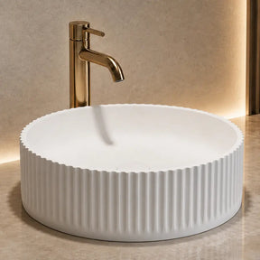 White ribbed solid surfaces sink on a marble countertop with a gold faucet