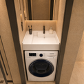 A Samsung front-load washing machine integrated beneath a white countertop sink with a chrome faucet in a tiled bathroom or laundry room.