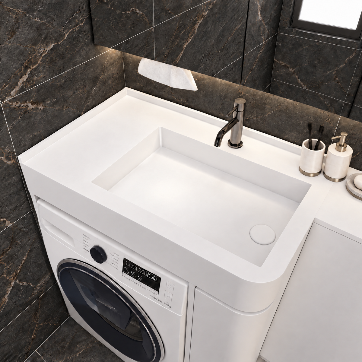 A white integrated sink vanity unit with a built-in washing machine, shown in a modern bathroom setting with dark marble wall and floor tiles.
